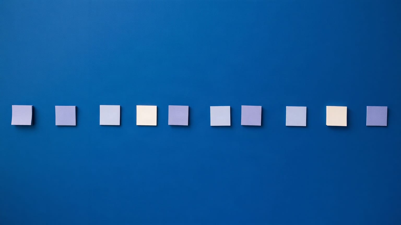 A row of small paper squares of the same size on a deep blue ground, most of them pale blue and two of them cream